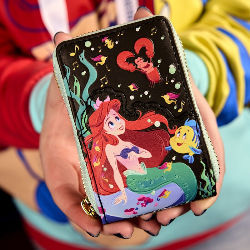 Two hands holding the Loungefly The Little Mermaid 35th Anniversary Life is the Bubbles Accordion Zip Around Wallet, featuring an image of Ariel, Sebastian, and Flounder on the front.